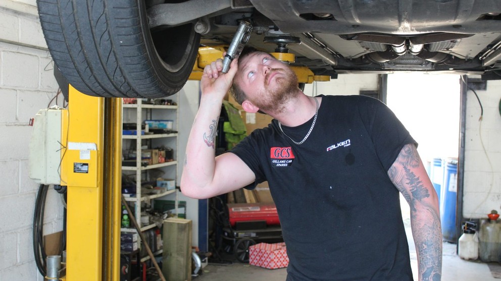 Mechanic under a car with a tool